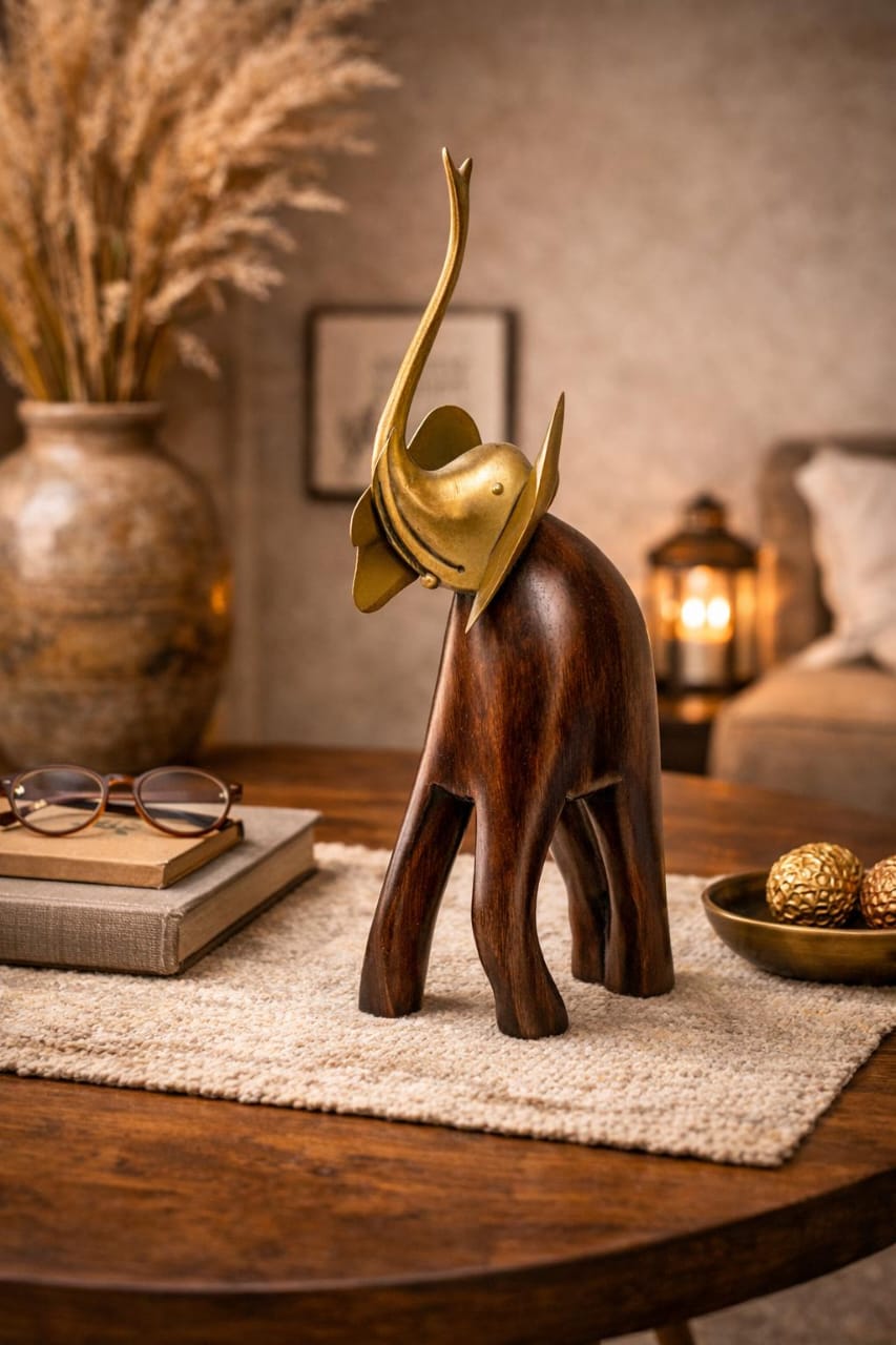 A decorative elephant figurine with a dark brown wooden body and a polished gold-colored horn, displayed on a round wooden table in a warm, styled room setting.